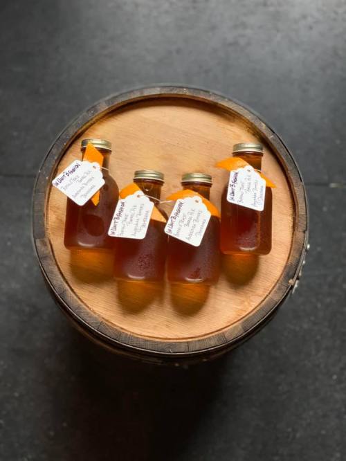 Four glass bottles filled with amber liquid, labeled and placed on a wooden barrel.