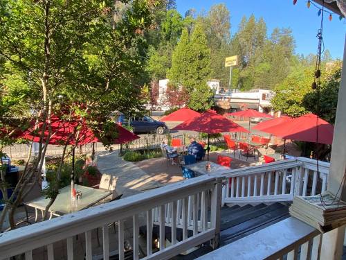 Outdoor dining area with red umbrellas, tables, and greenery, set in a scenic location with trees and a nearby road.