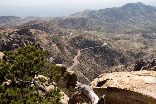 A winding road snakes through rugged mountains, with rocky terrain and sparse vegetation under a clear sky.