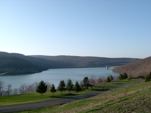 A serene lake surrounded by rolling hills and trees under a clear blue sky.
