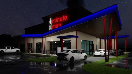 A modern building with "Minute Man" signage, illuminated at night, featuring a parking lot and several parked cars.