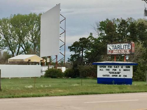 A drive-in theater sign with a large screen and a marquee advertising weekend events and movie showings.