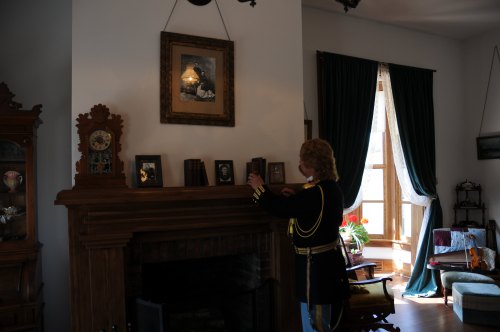 A person in a historical uniform adjusts photos on a mantel in a warmly lit room with vintage decor.