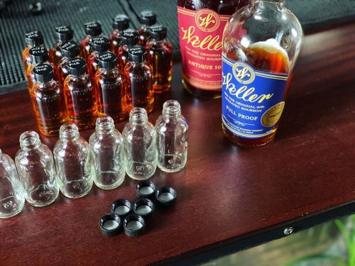 A wooden surface with several whiskey bottles, including Weller Antique 107 and Full Proof, alongside empty glass vials.