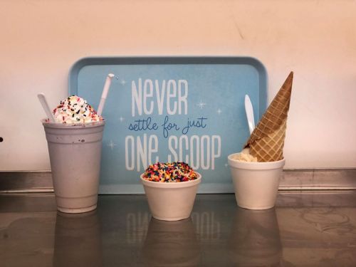 Three ice cream treats: a milkshake, a cup with sprinkles, and a cone, with a sign that says "Never settle for just one scoop."
