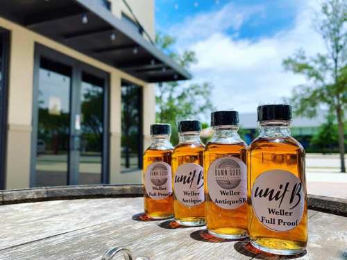 Four small bottles of whiskey labeled "Weller Antique" and "Weller Full Proof" on a wooden table outdoors.