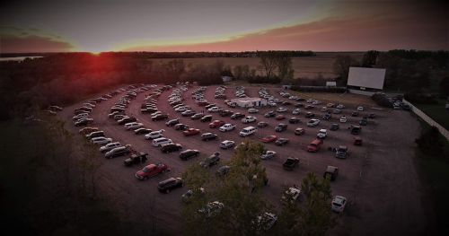 Aerial view of a drive-in movie theater at sunset, with numerous cars parked in a circular layout.