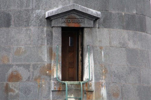 A weathered stone tower with a wooden door and a ladder, marked "A D 1860" above the entrance.