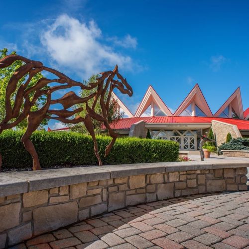 A horse sculpture in front of a modern building with triangular red roofs and landscaped greenery.