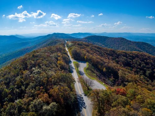 Aerial view of a winding road through colorful autumn mountains under a clear blue sky.