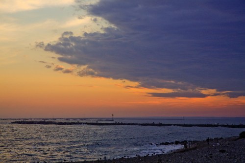A serene sunset over the ocean, with dark clouds contrasting against a warm orange and purple sky.