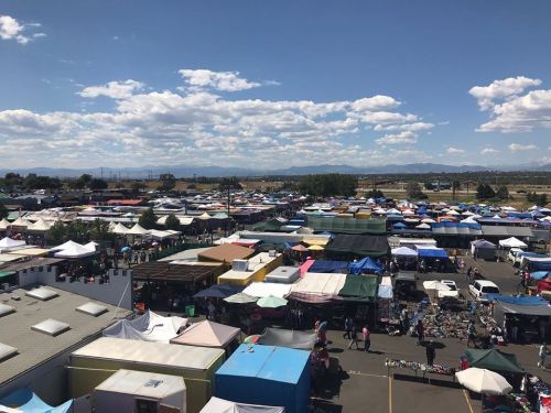 Aerial view of a vibrant outdoor market with colorful tents and stalls under a blue sky with scattered clouds.