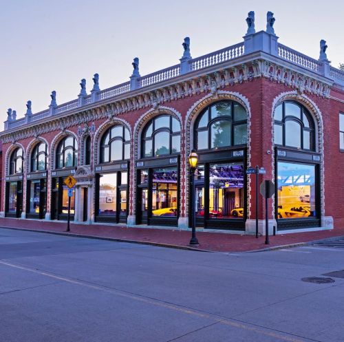 Historic brick building with arched windows, decorative details, and a streetlamp, illuminated at dusk.