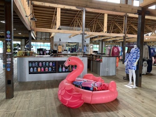 A bright pink flamingo float sits in a store filled with clothing and merchandise, featuring wooden beams and a spacious layout.