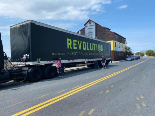 A large black truck with "REVOLUTION Event Design and Production" printed on the side parked on a street near a building.