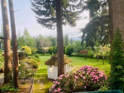 A serene garden scene featuring a gazebo surrounded by lush greenery and blooming flowers under tall trees.