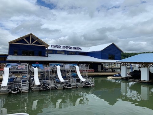 A marina with blue buildings and boat slips on a calm lake under a cloudy sky.