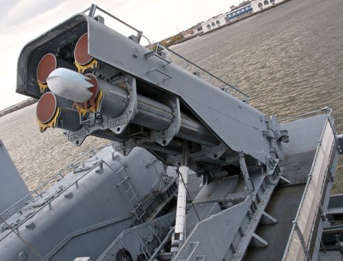 A close-up of a missile launcher on a naval vessel, positioned over water with a cloudy sky in the background.