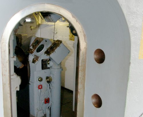 A view through a circular doorway into a submarine's control room, featuring dials and levers.