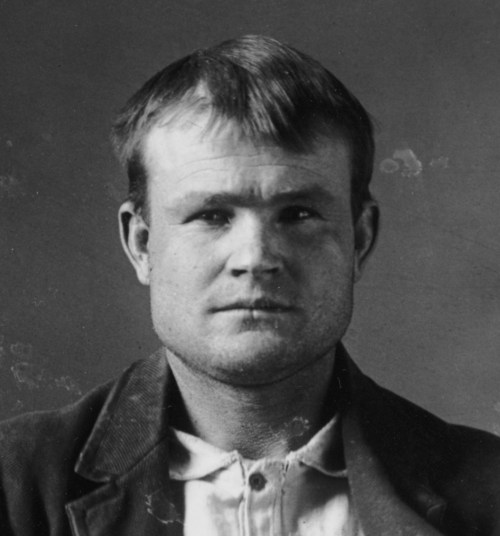 Black and white portrait of a man with short hair, wearing a jacket and shirt, looking directly at the camera.