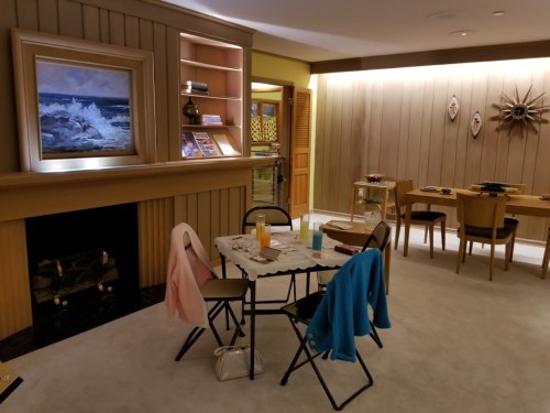 Cozy room with a fireplace, artwork, and a dining area featuring chairs and a table set for drinks.
