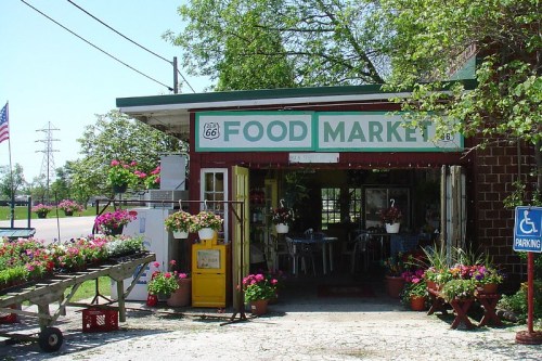 A charming food market on Route 66, featuring flowers, outdoor seating, and a welcoming entrance.