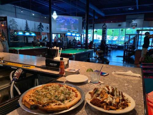 A bar scene featuring a pizza and loaded fries on the counter, with a pool table and a large TV in the background.