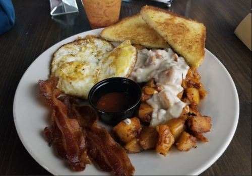 A plate of breakfast featuring eggs, bacon, toast, and a side of seasoned potatoes with gravy.
