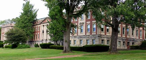 Historic brick building surrounded by trees and manicured lawns on a sunny day.
