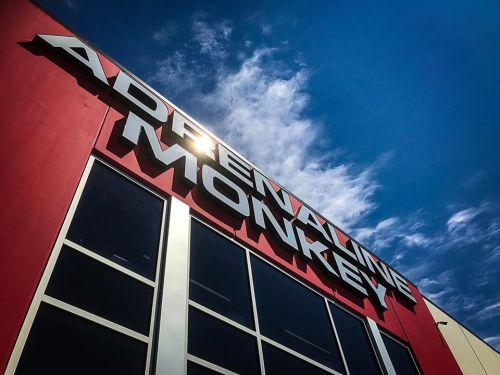 A building with a red exterior featuring the sign "Adrenaline Monkey" against a blue sky with clouds.