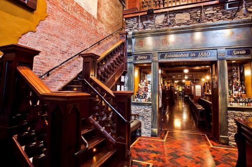 Interior of a historic bar with wooden stairs, stone walls, and a warm, inviting atmosphere.