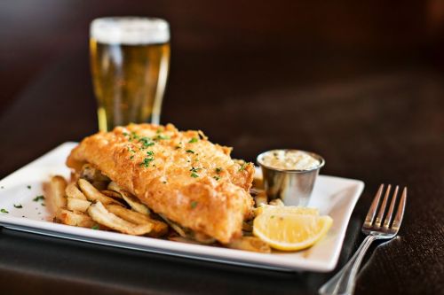 A plate of golden fried fish with fries, a lemon wedge, and tartar sauce, alongside a glass of beer.