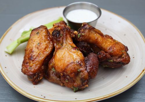 A plate of crispy chicken wings with a side of ranch dressing and celery sticks.