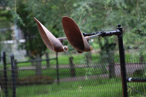 Two large, rusted metal blades mounted on a pole, set against a green, blurred background.