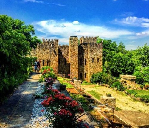 A stone castle surrounded by lush greenery and colorful flowers under a bright blue sky.