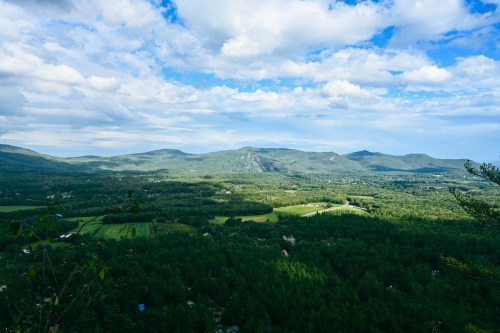 A panoramic view of lush green mountains and valleys under a partly cloudy sky.