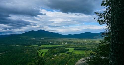 A panoramic view of rolling green hills and mountains under a cloudy sky.