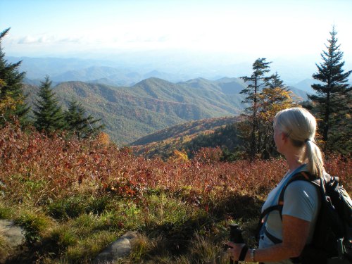 A hiker with a backpack gazes at a scenic mountain view filled with autumn foliage.