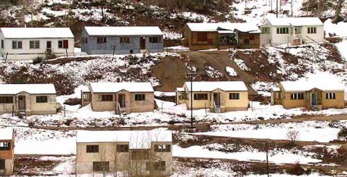 A row of colorful houses on a snowy hillside, surrounded by trees and a winter landscape.