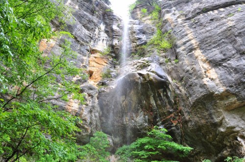 A waterfall cascades down rocky cliffs, surrounded by lush green trees and vegetation.