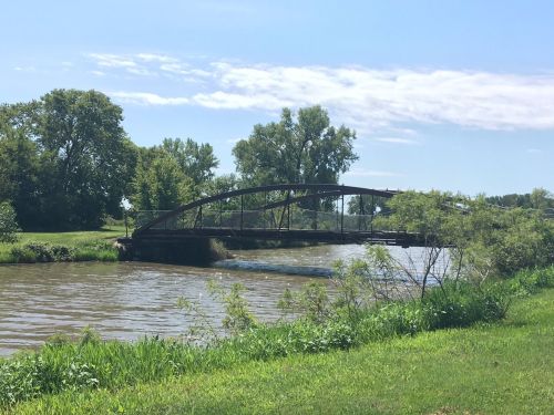 A serene river scene featuring a bridge surrounded by lush greenery under a clear blue sky.