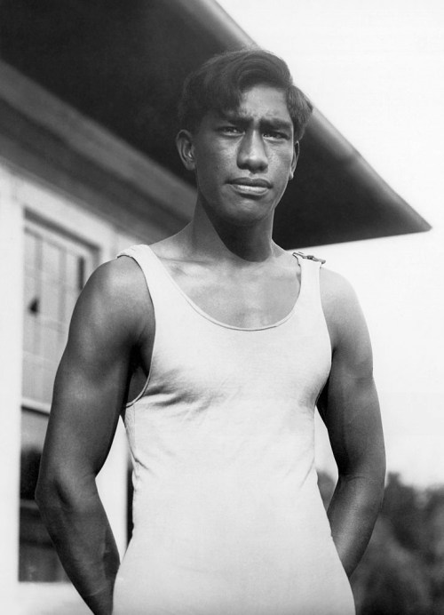 A young man in a sleeveless shirt stands confidently outdoors, with a building in the background.