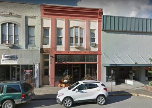 A quaint street scene featuring a red brick building with "Farm Market" signage and a white car parked in front.