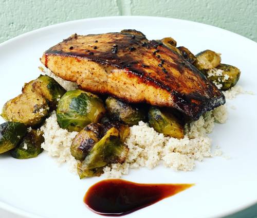 Grilled salmon fillet on a bed of couscous, served with roasted Brussels sprouts and a drizzle of sauce.