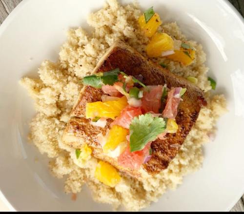A plate of couscous topped with a seared fish fillet and a citrus salsa of grapefruit and orange, garnished with cilantro.