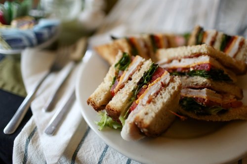 A plate of sliced sandwiches with layers of turkey, bacon, lettuce, and tomato, served on a striped tablecloth.