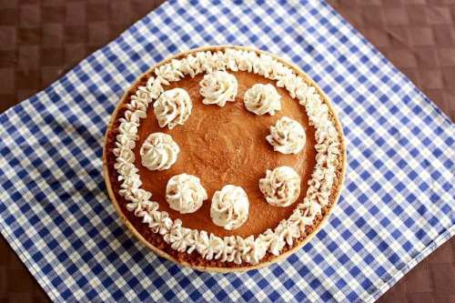 A pumpkin pie topped with whipped cream rosettes, placed on a blue and white checkered cloth.