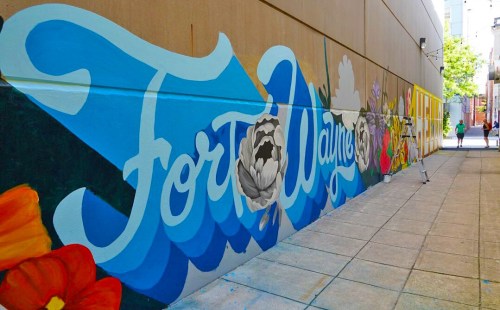 Colorful mural featuring the text "Fort Wayne" surrounded by flowers, set against a city backdrop.