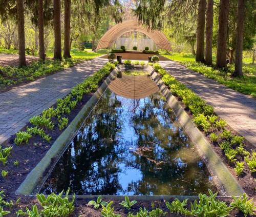 A serene garden scene featuring a reflecting pool surrounded by greenery and a modern pavilion in the background.