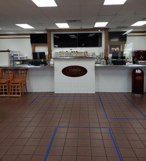 Interior of a restaurant with a counter, seating area, and tiled floor marked with blue tape.